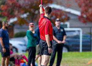 Referee in red raising flag to indicate which team has the ball.