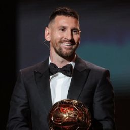 Messi on stage smiling and holding trophy after winning the 2023 balloon d'or