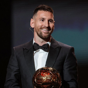 Messi on stage smiling and holding trophy after winning the 2023 balloon d'or