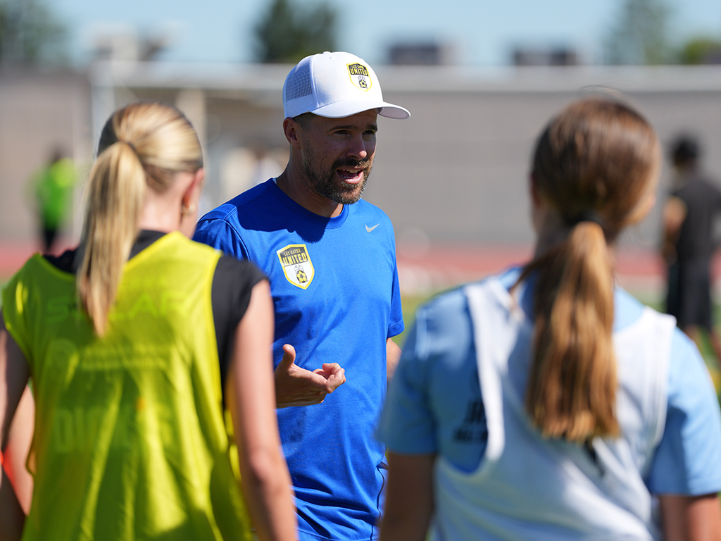 An LGU coach talking with two players on the field during summer programs in 2026.