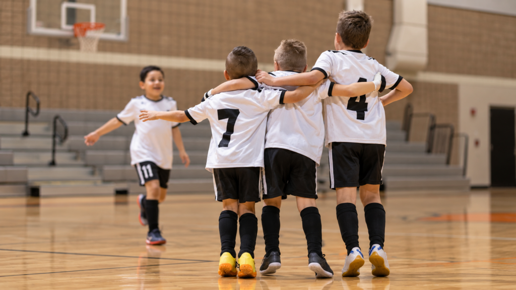 Illustrative image of youth futsal teammates celebrating in a school-style gym.