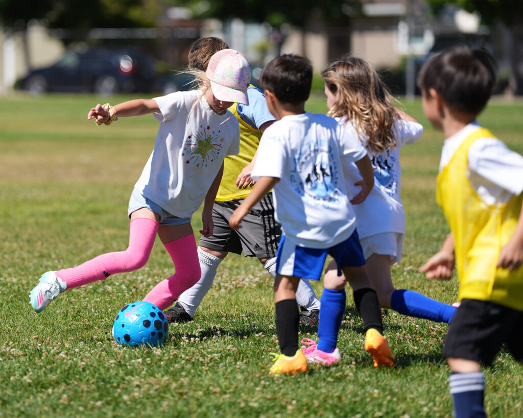 Young campers playing soccer together around a blue ball at LGU Summer Soccer Camp in 2026.